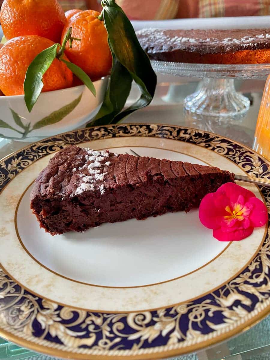 porcelain plate with a slice of moist chocolate cake, an edible begonia flower and bowl of clementine oranges