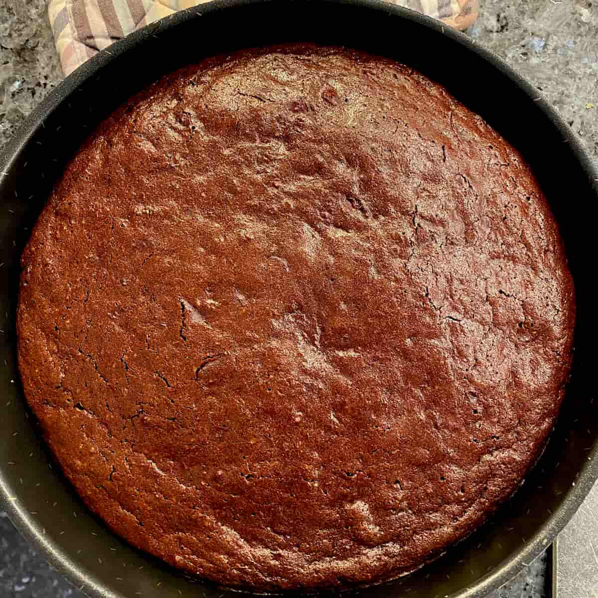 perfectly round and flat chocolate cake in metal tin just out of the oven