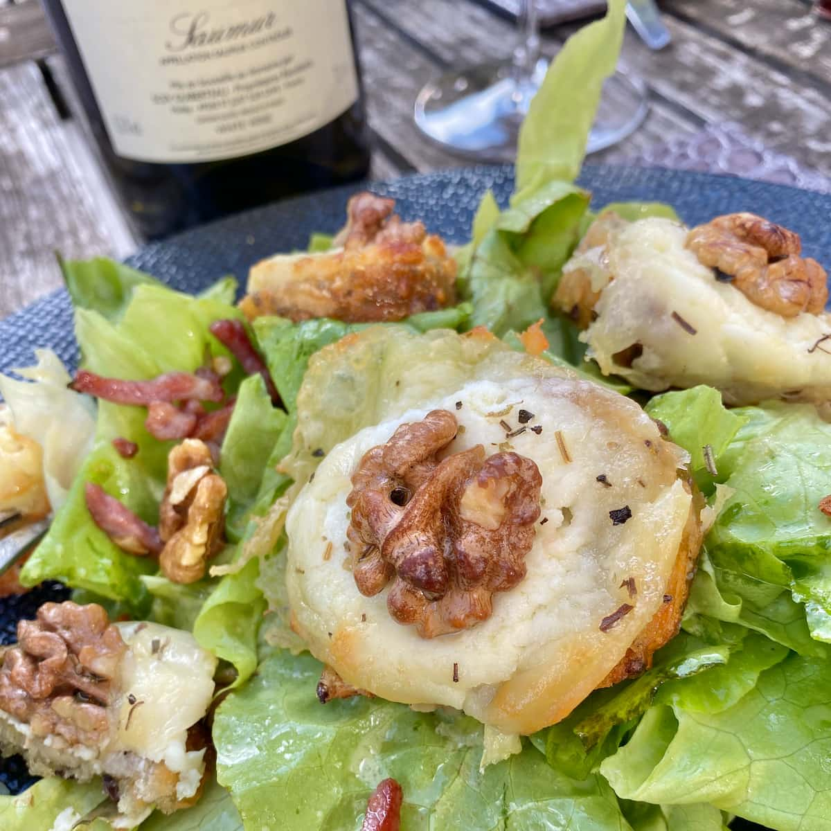 grilled cheese and walnuts on small baguette toasts on top of a green salad with bacon