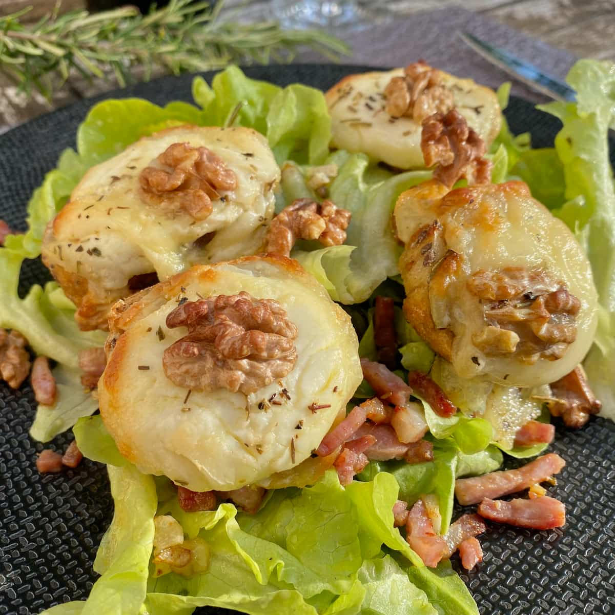 slices of toasted baguette French bread topped with grilled cheese and walnuts on a bed of dressed lettuce and bacon bits