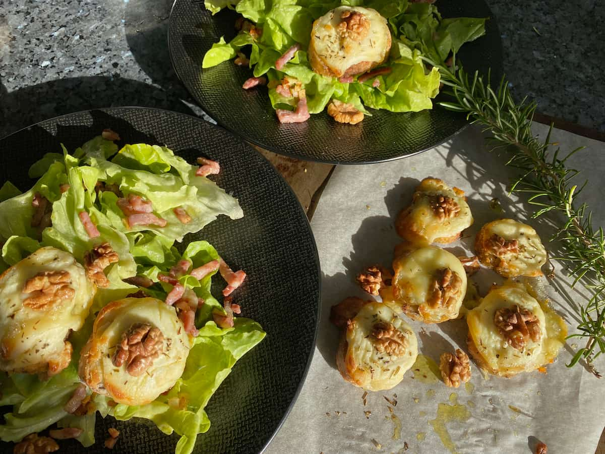 plates of lettuce and bacon topped with slices of baguette and grilled cheese with walnuts