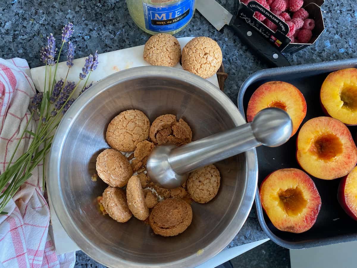 crushing amaretti cookies in a mortar and pestle surrounded by peach halves