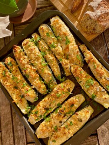 baking tray of stuffed zucchini boats topped with cheese, breadcrumbs, nuts and herbs