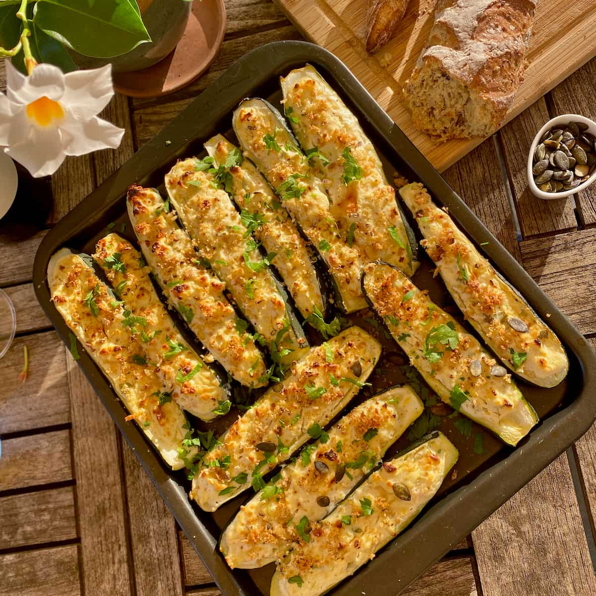 baking tray of stuffed zucchini boats topped with cheese, breadcrumbs, nuts and herbs