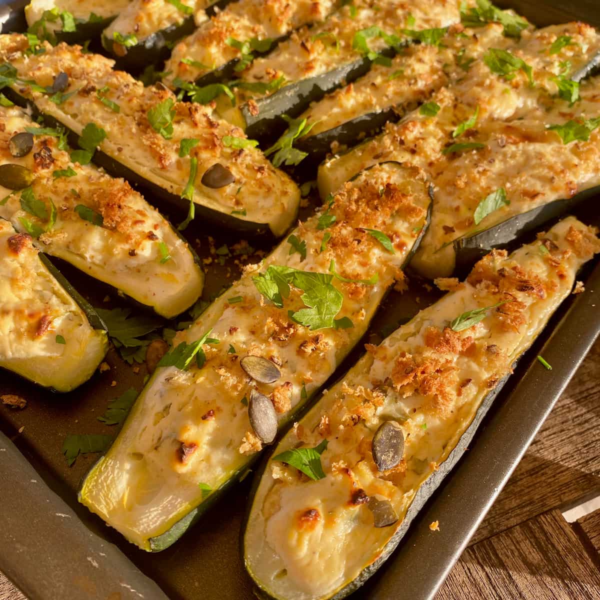 rows of zucchini boat halves topped with cheese, breadcrumbs, seeds and herbs