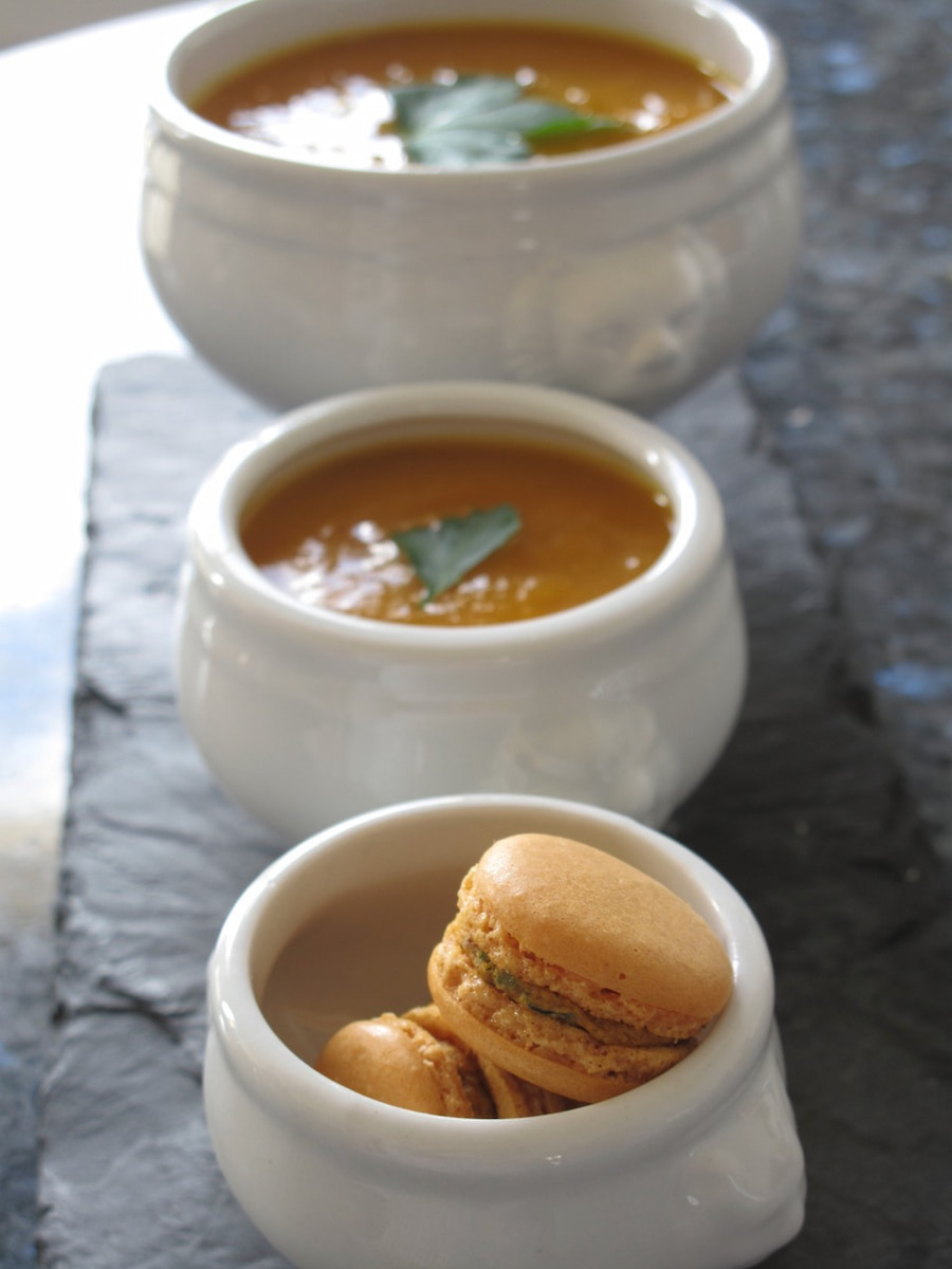 3 different sized white French lion bowls of soup with one of macarons