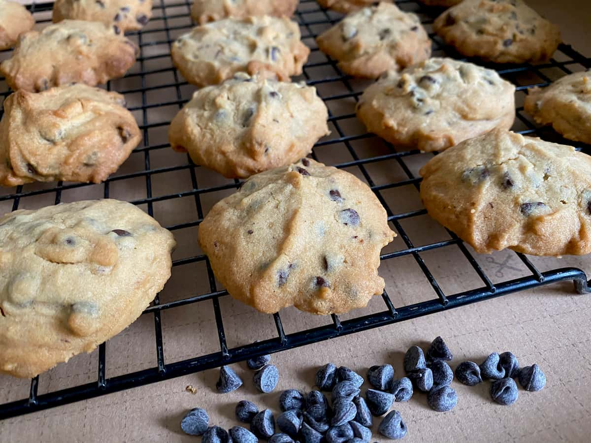 golden brown cookies cooling on a wire tray with a pile of chocolate chips