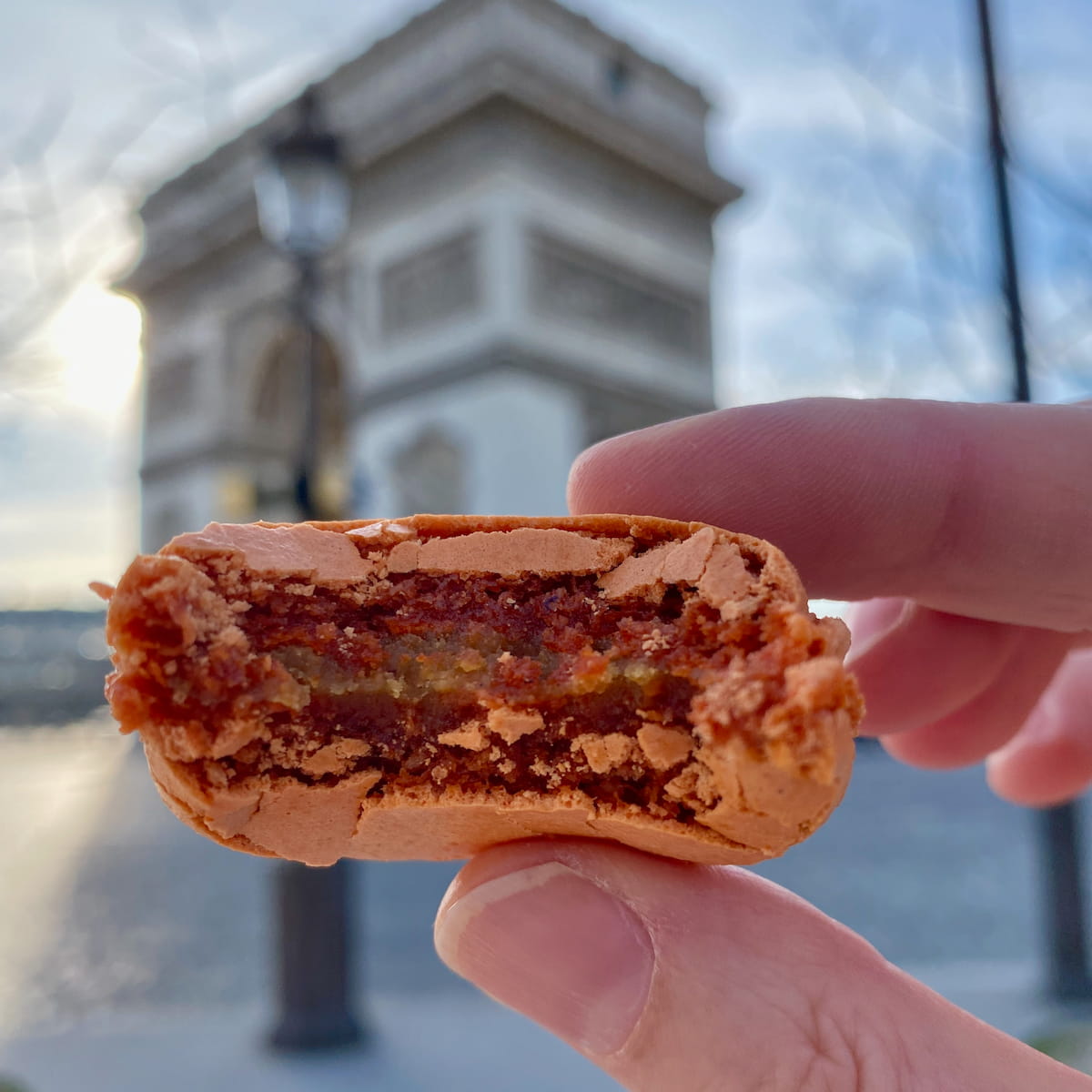 biting into a fondant and crispy macaron in front of the Arc de Triomphe in Paris