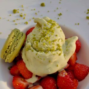 large dessert bowl with strawberries topped with light green ice cream topped with ground pistachio nuts and macaron