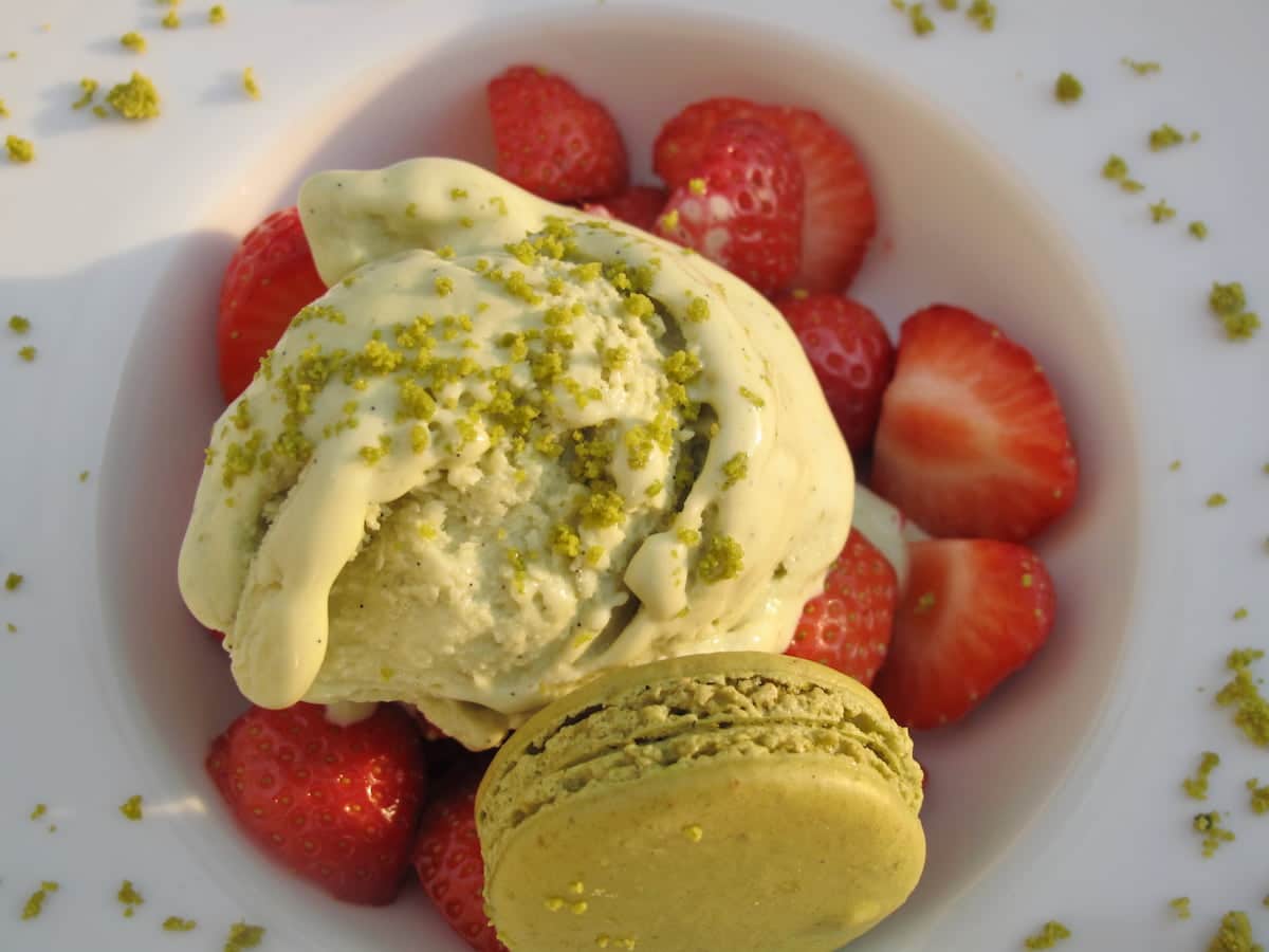 creamy ice cream topped with pistachios with macaron and strawberries