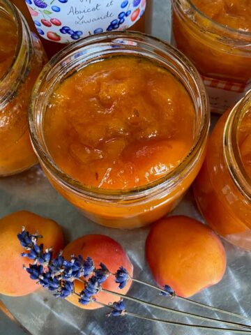 glass jars filled with bright orange apricot jam with sprigs of purple lavender