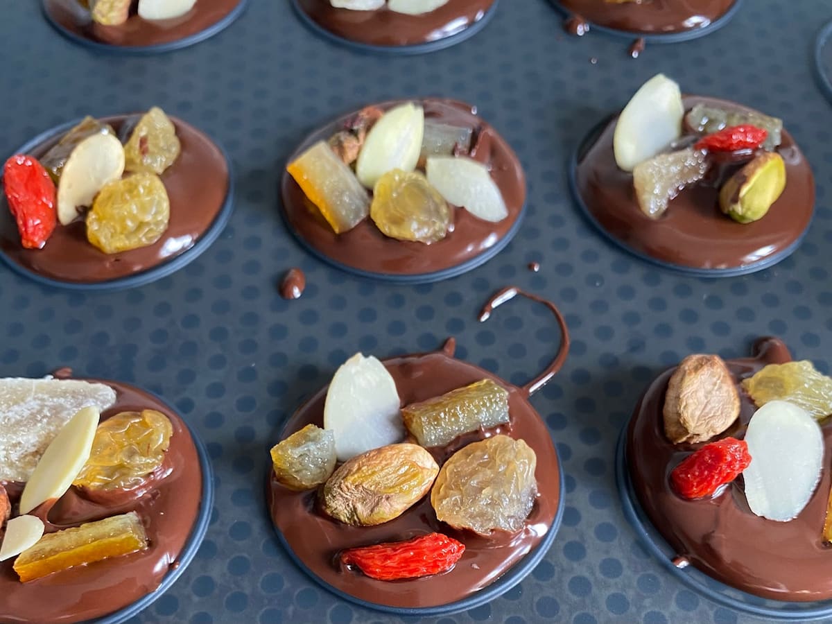 melted chocolate topped with dried fruit and nuts on a silicone mat with disks