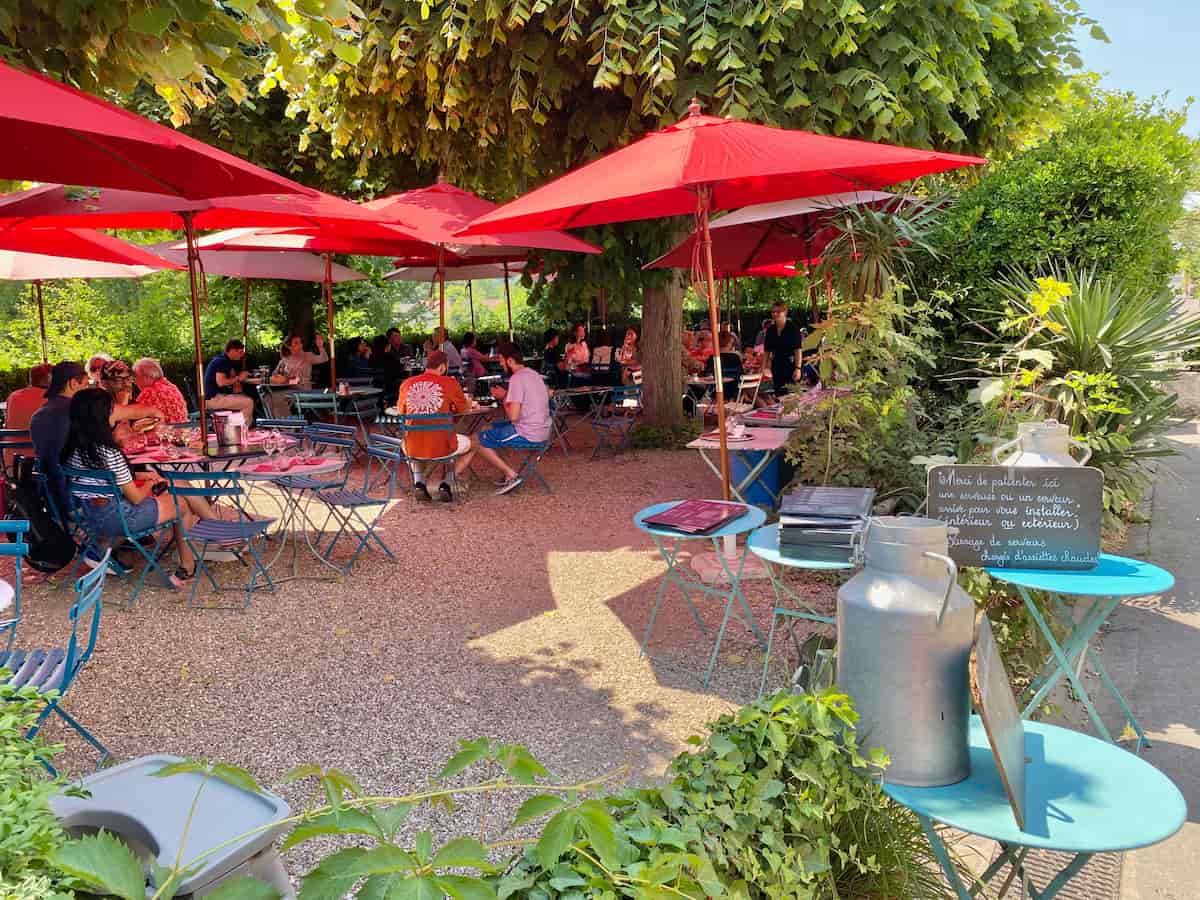 shady restaurant outside with trees and red umbrellas