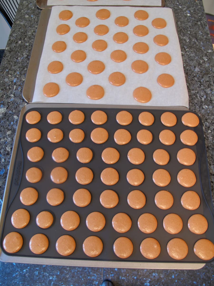 piped out macaron batter on paper and on a silicone baking mat to compare