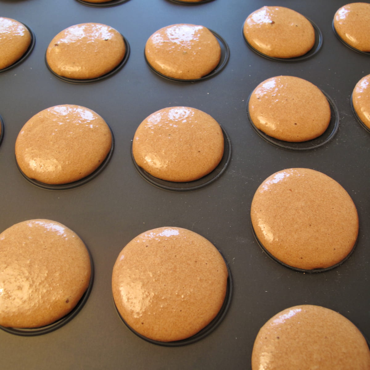 piped out macaron batter on to a black silicone mat