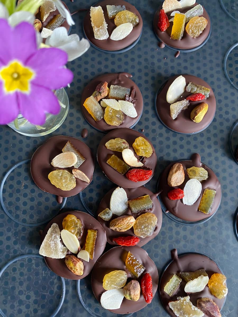 round chocolate disks topped with fruit and nuts on a baking mat