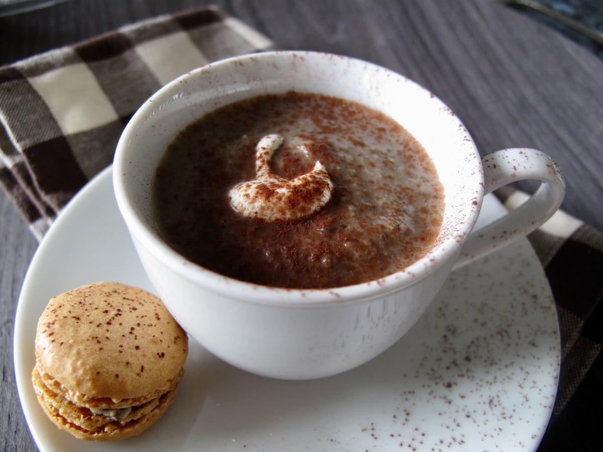 cup and saucer of mushroom soup, dollop of cream, dusting of cocoa powder and a mini mushroom macaron