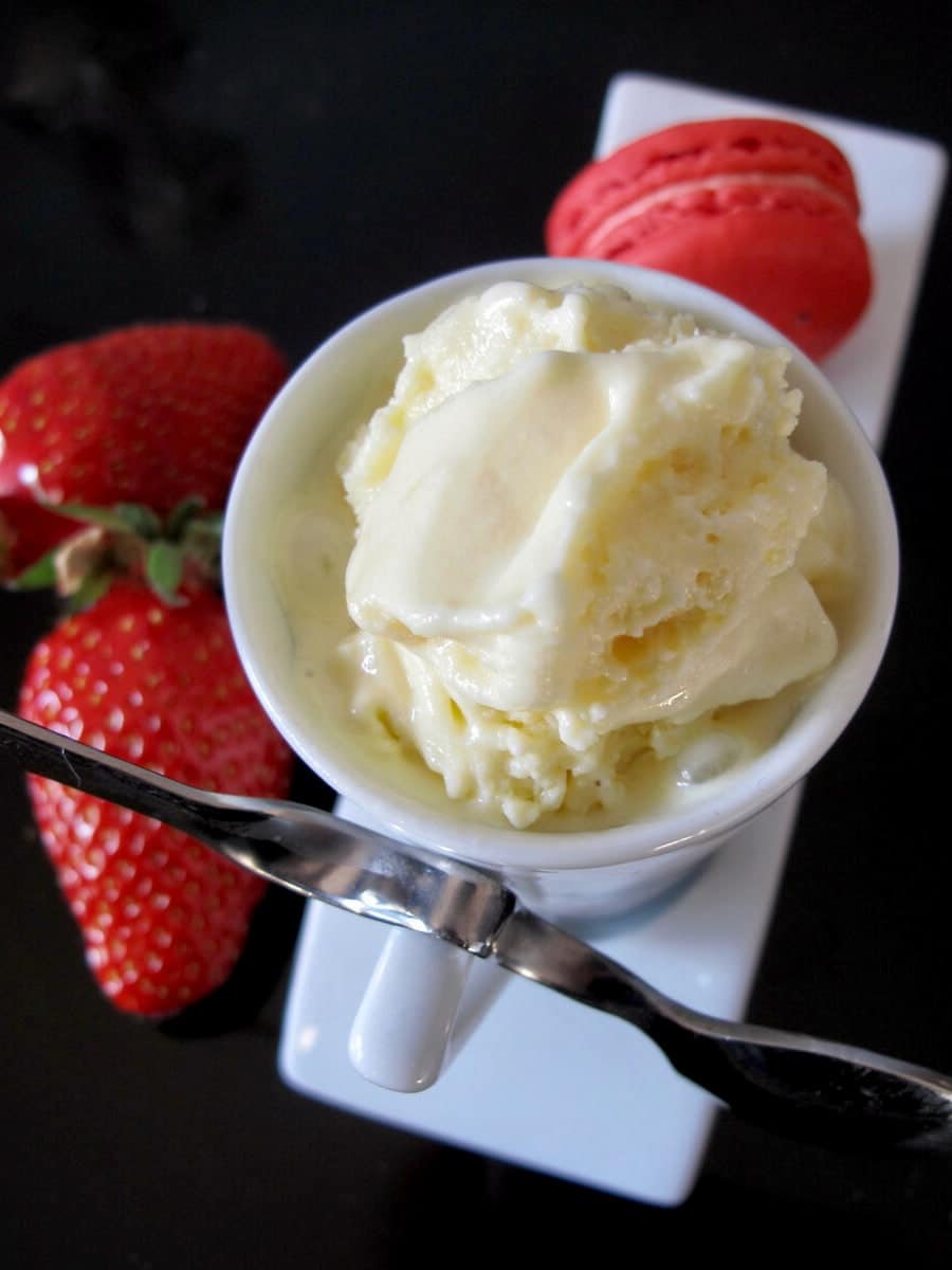 cup of creamy ice cream starting to melt, next to strawberries and a red French macaron