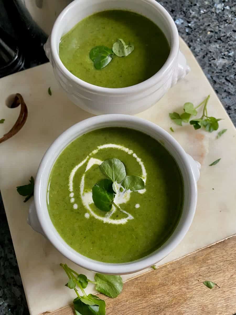 bowls of green watercress soup with a swirl of cream and topped with watercress leaves