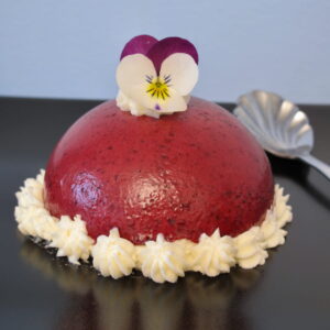 dark red-purple dome topped with an edible pansy and piped cream around the bottom