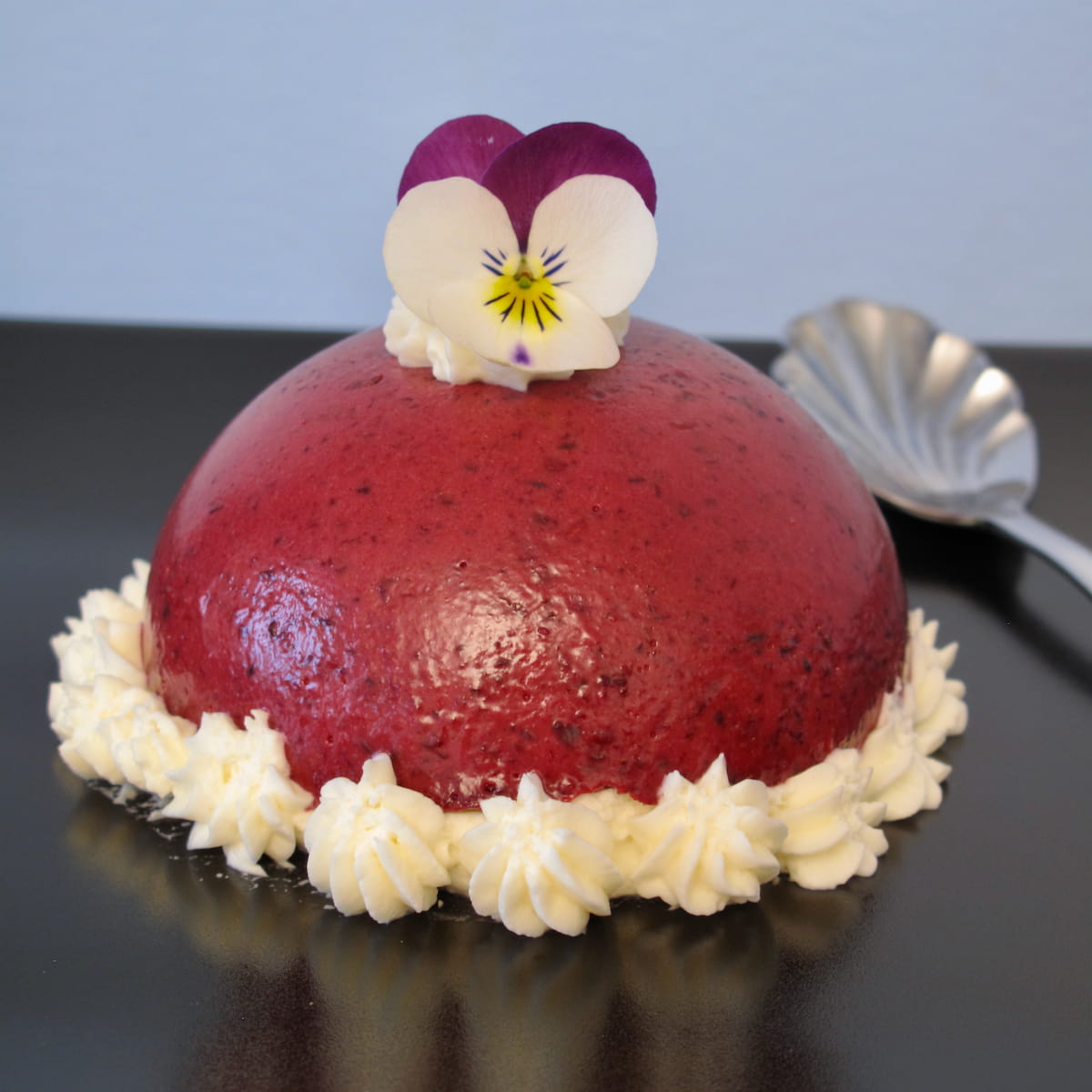 sexy valentine macaron dessert dark red-purple dome topped with an edible pansy and piped cream around the bottom