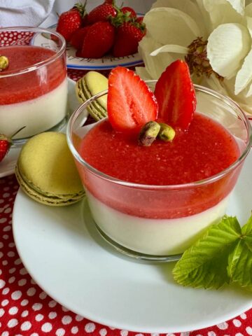 glass dessert dish of creamy pistachio panna cotta topped with a strawberry coulis