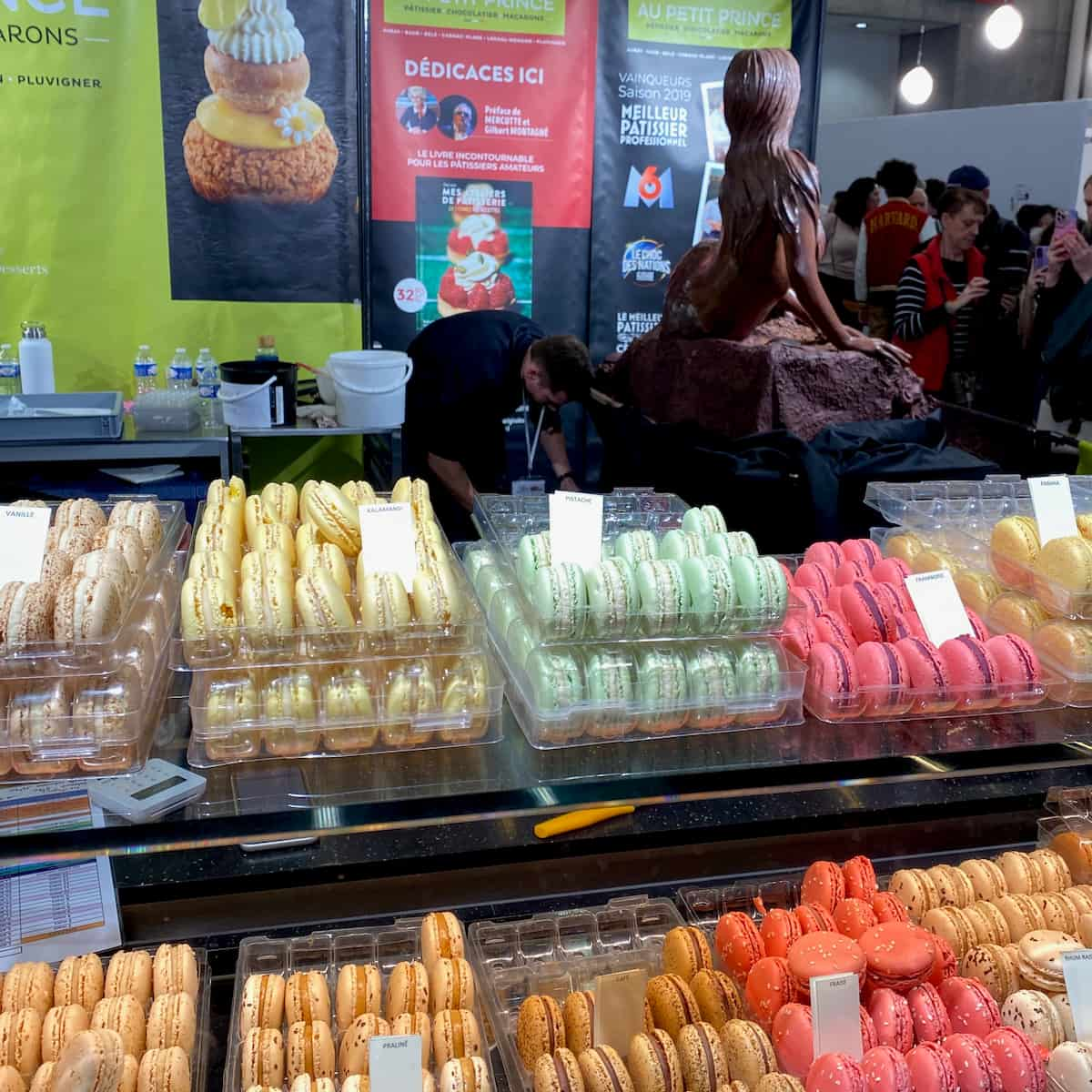 rows of pastel coloured macarons in front of a chocolate mermaid sculpture