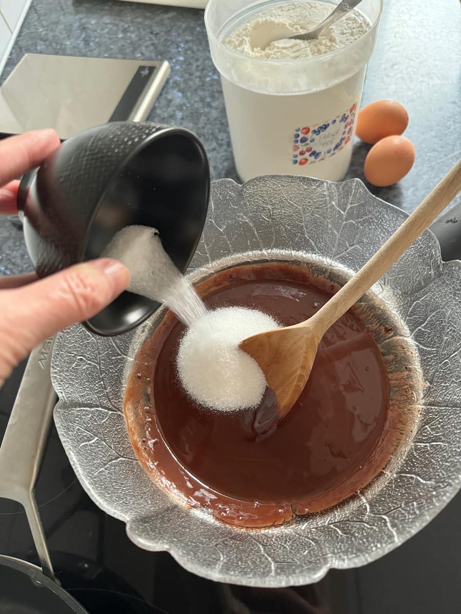 pouring a little sugar into a melted chocolate mix
