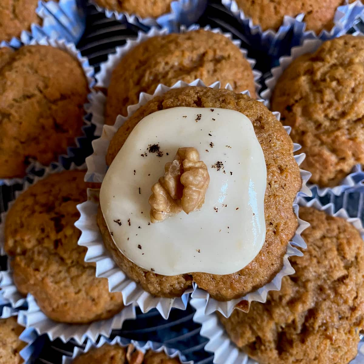 stack of muffins in paper cases with one topped with icing, vanilla flecks and a walnut