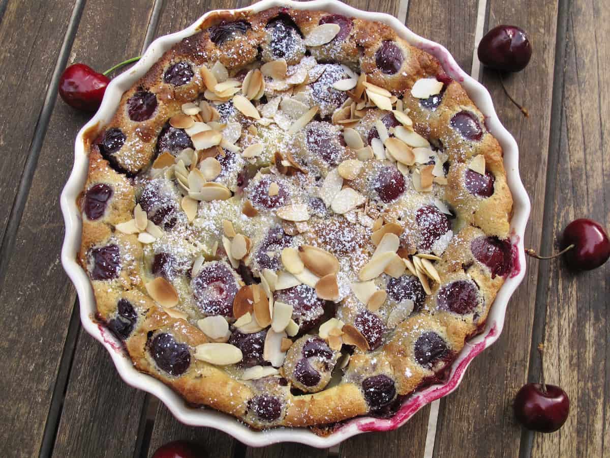 cherry clafoutis baked in dish topped with toasted almonds on rustic wooden table