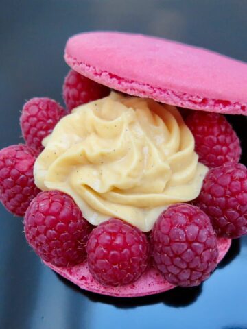 large pink macaron with pastry cream with a border of raspberries