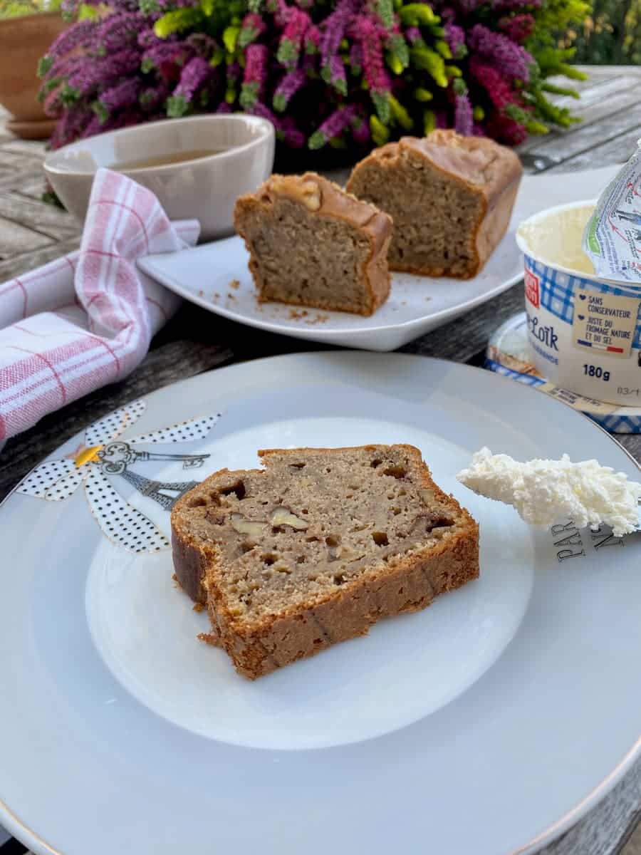 spreading cream cheese on a slice of moist banana bread with coffee