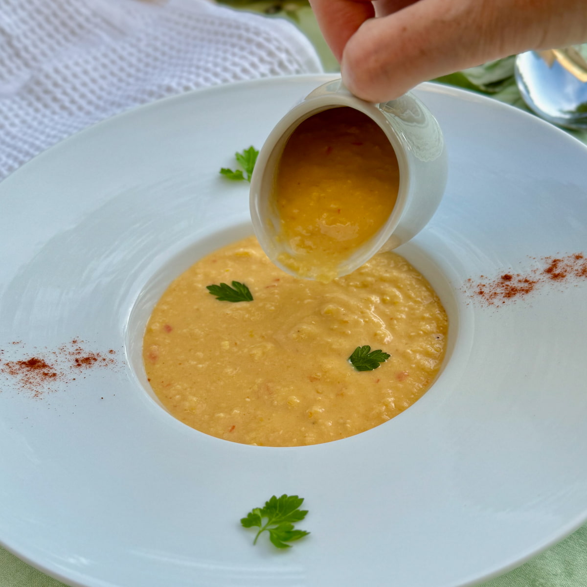 large rimmed porcelain restaurant dish with thick and creamy corn chowder, served from a little jug