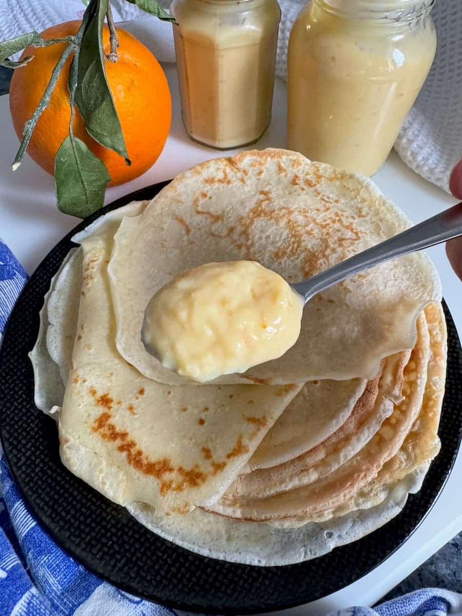 a large spoon of creamy orange curd on a pile of thin crêpes