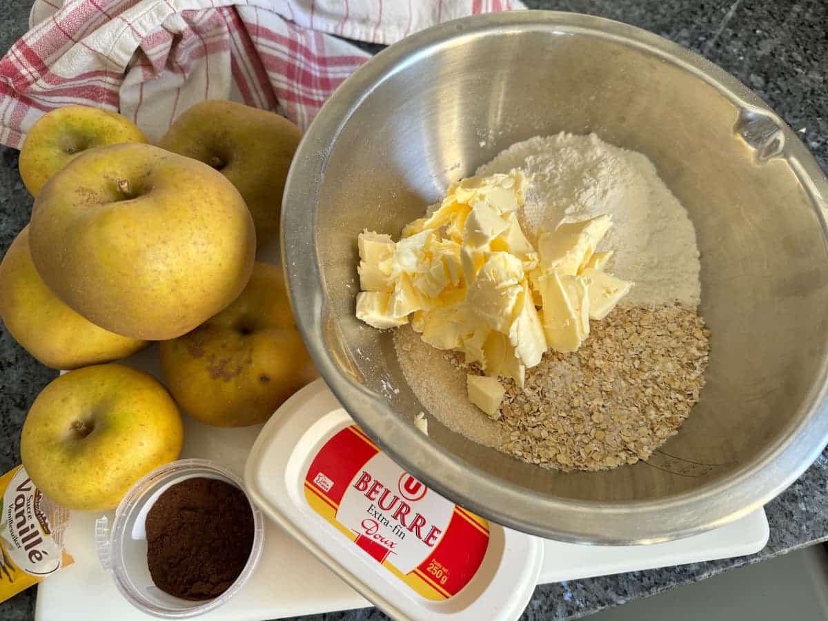 bowl of flour, oats, sugar and cubes of butter next to apples