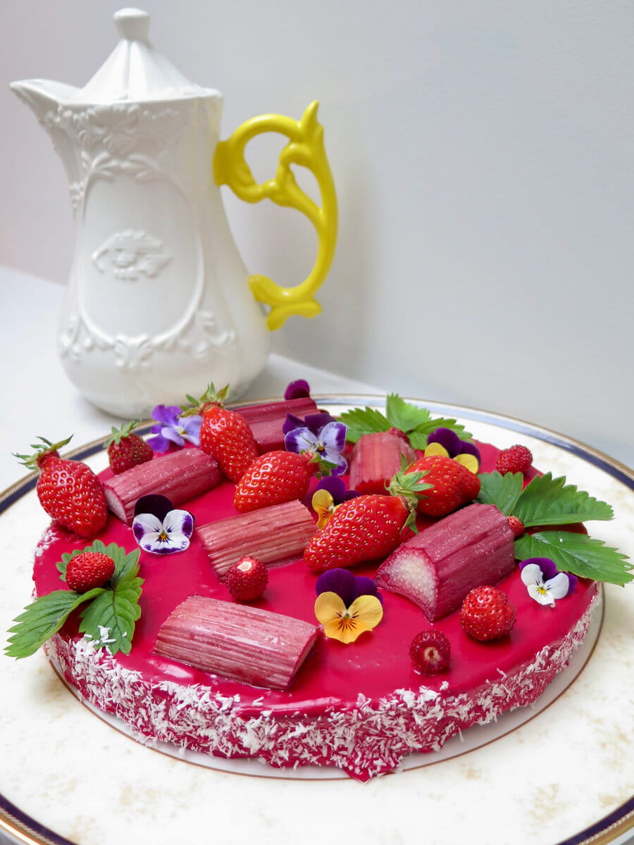 deep pink glazed cake topped with roasted rhubarb, strawberries and pansies