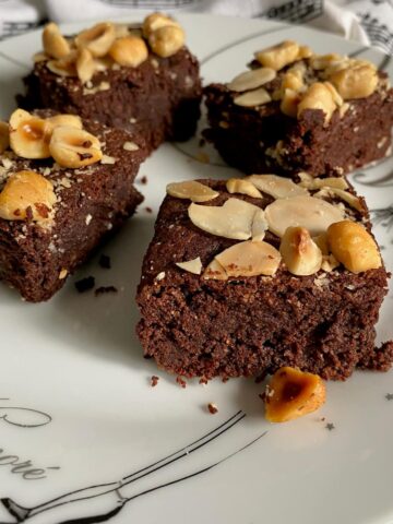 gluten free brownie squares topped with toasted almonds and hazelnuts on a French plate