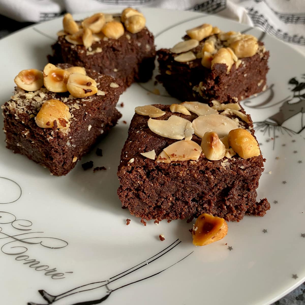 gluten free brownie squares topped with toasted almonds and hazelnuts on a French plate