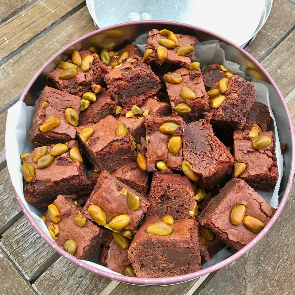 a tin of fudgy brownie squares topped with toasted green pistachio nuts