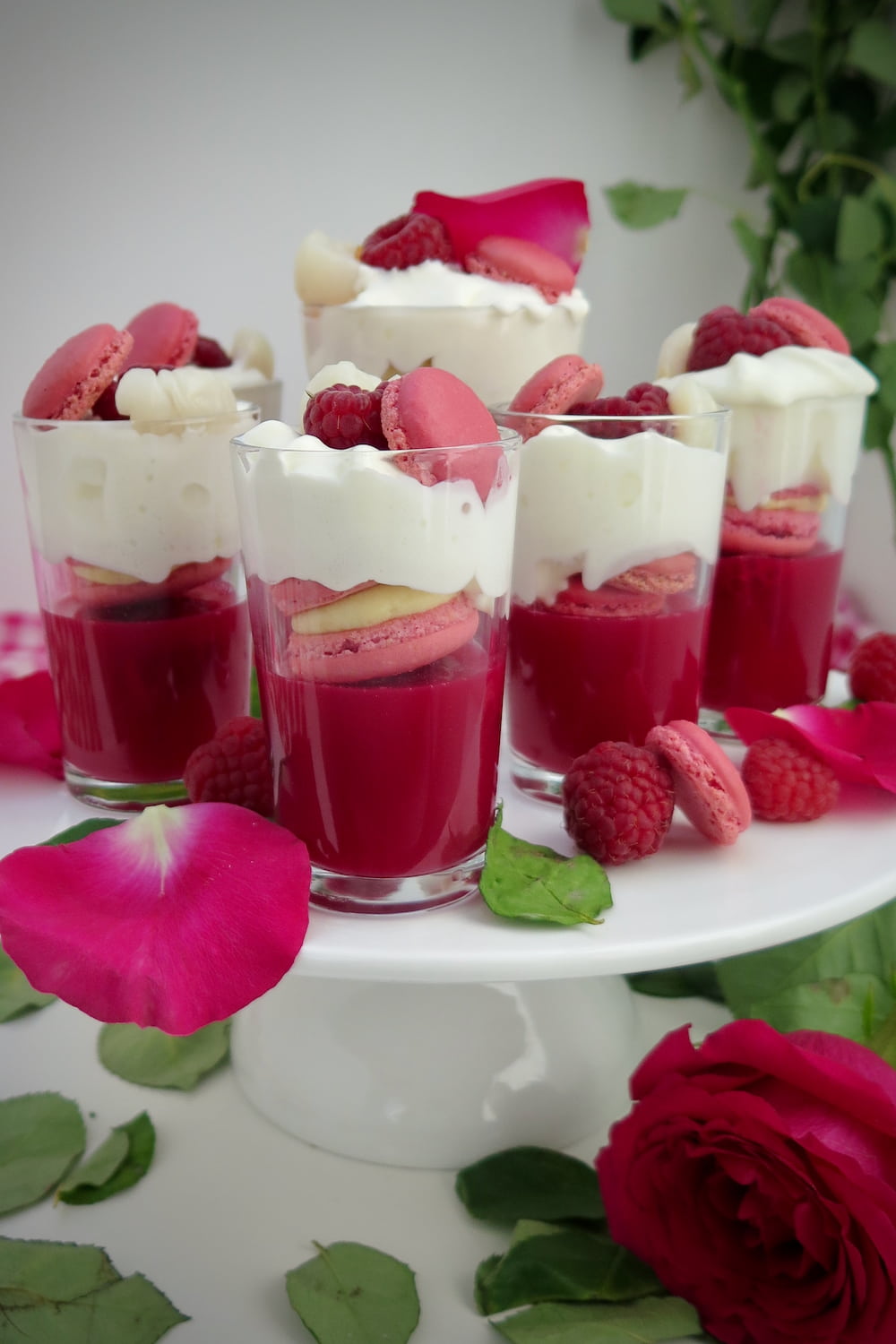 glass shot glasses with deep pink trifles topped with pink macarons, rose petals and raspberries