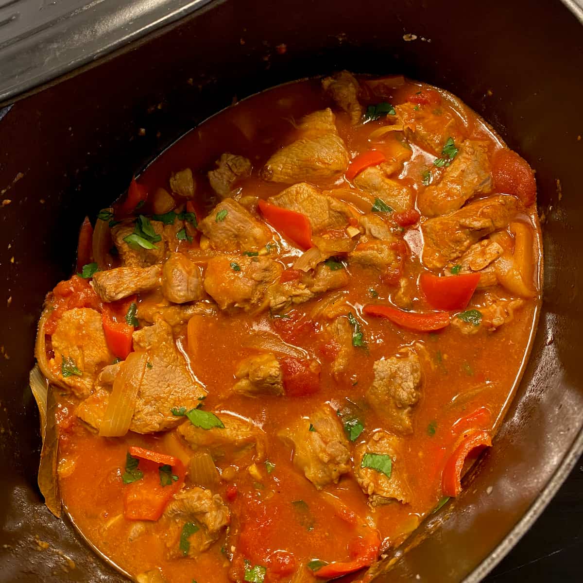 vibrant red tomato bubbling sauce with veal and vegetables in a crock pot