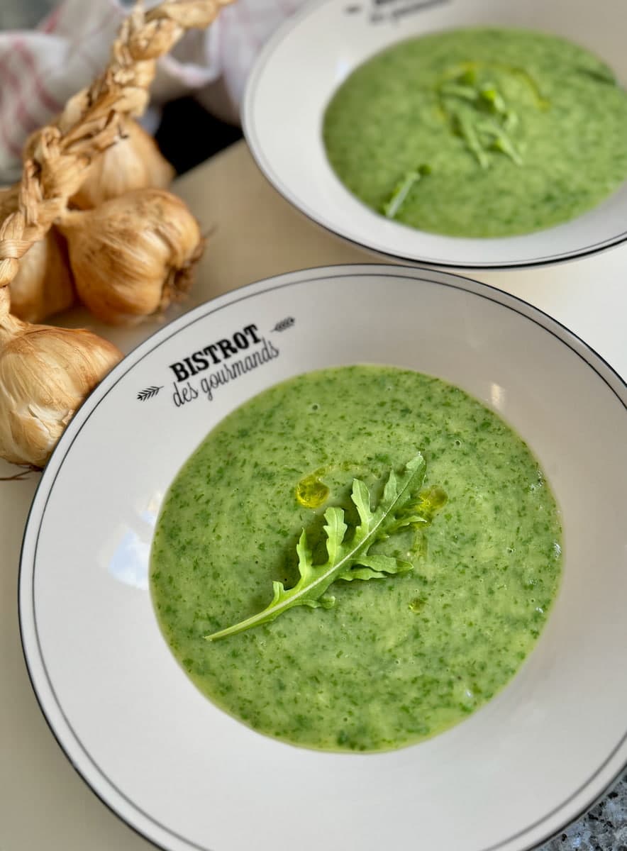 bowls of bright green soup topped with rocket leaves (arugula) and smoked garlic