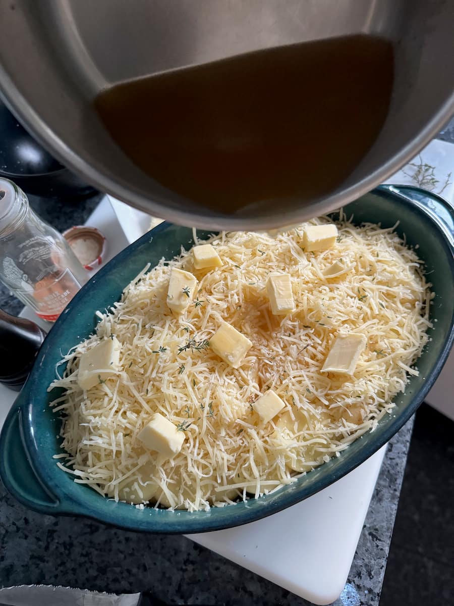pouring chicken stock over potatoes, cheese, butter and thyme herb