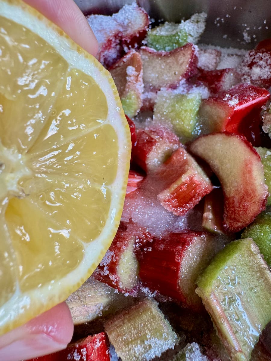 squeezing a large juicy lemon into a pan of rhubarb and sugar
