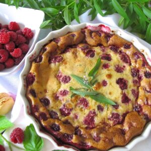 raspberry clafoutis in an ovenproof dish topped with lemon verbena leaves served with a vanilla macaron