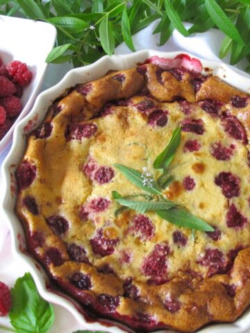 raspberry clafoutis in an ovenproof dish topped with lemon verbena leaves served with a vanilla macaron