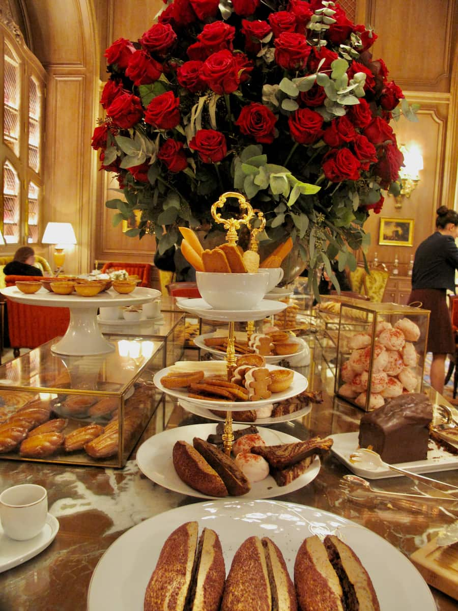 plates of cakes on a marble table next to a huge bouquet of red roses