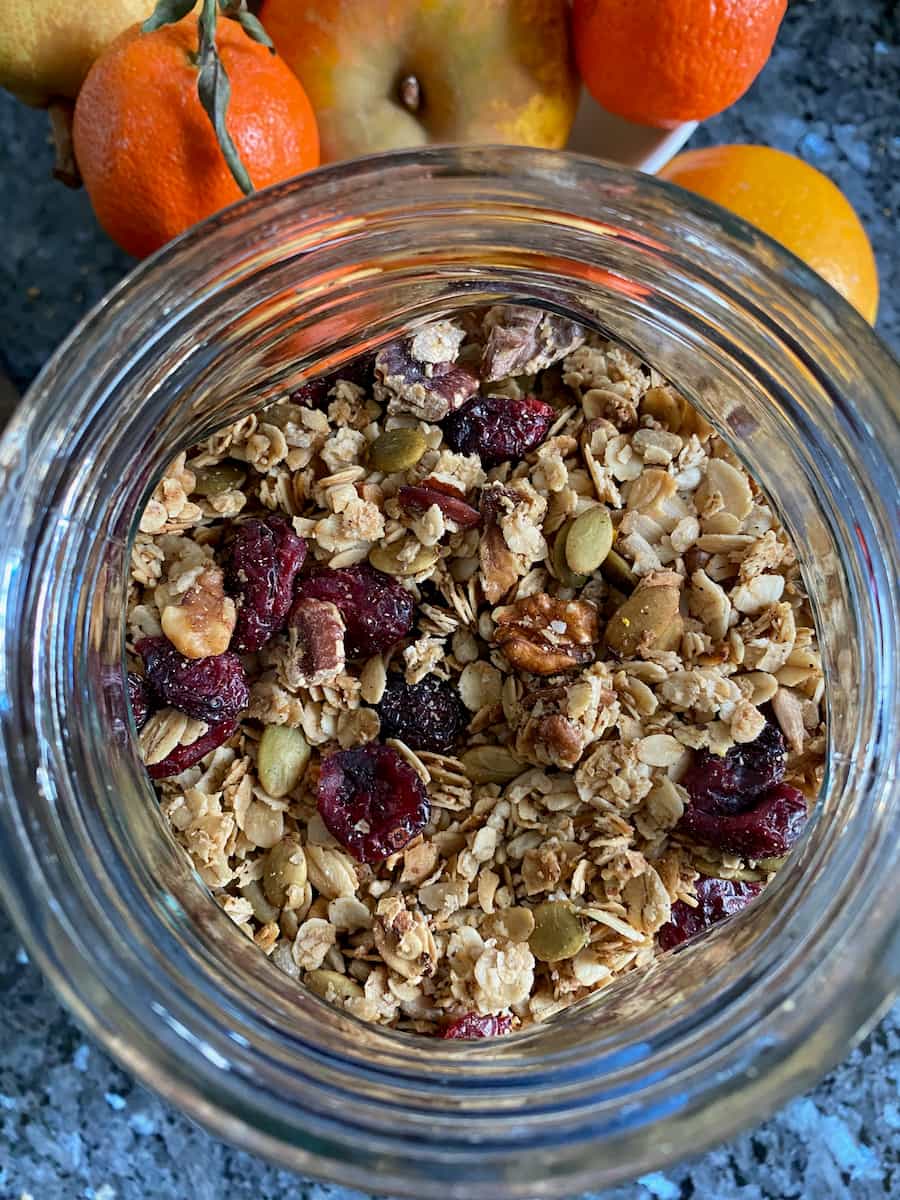 looking down into a cookie jar filled with crispy spiced granola with red cranberries, nuts and orange