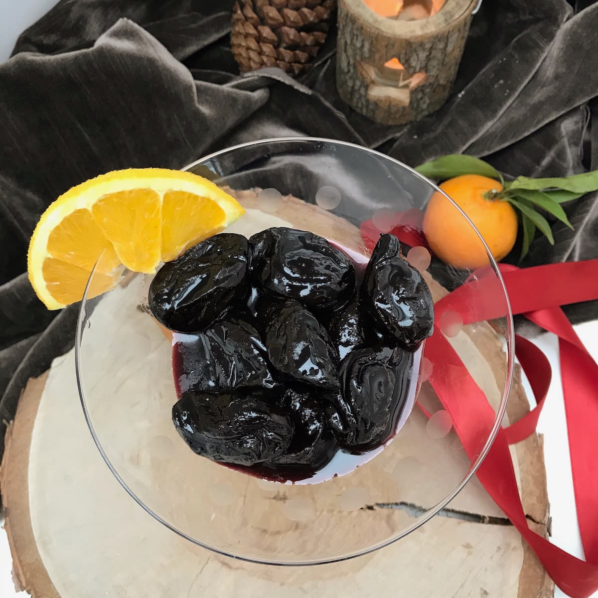 glass dish with prunes in wine and orange wedge