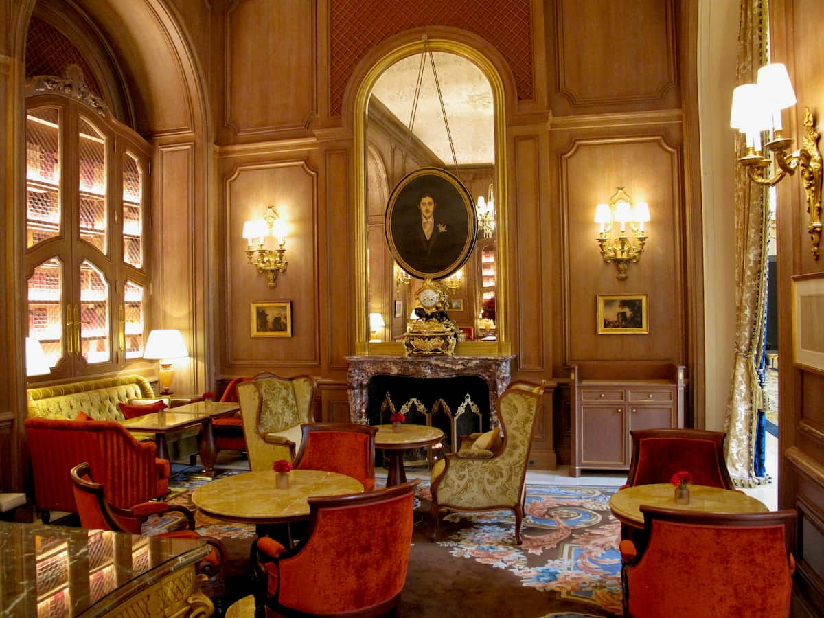 Portrait of Marcel Proust above the chimney in a chic room with armchairs and marble tables